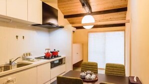 A compact kitchen with white cabinets, a stove, and a sink. There is a dining area with a table and chairs. - Kyoto Tanbaguchi Classic Japanese House (Kyoto)
