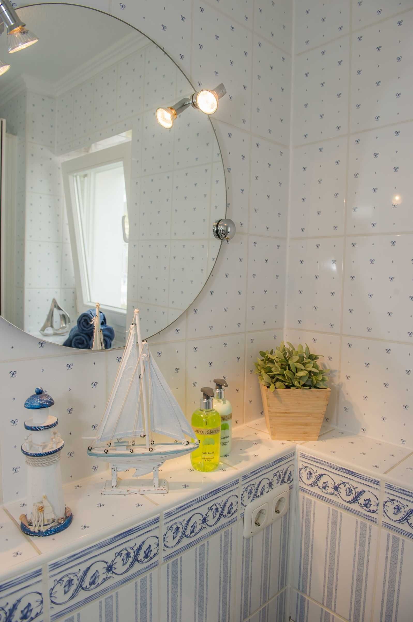 Casa de banho com espelho redondo, decoração náutica, planta em vaso e produtos de higiene no balcão.