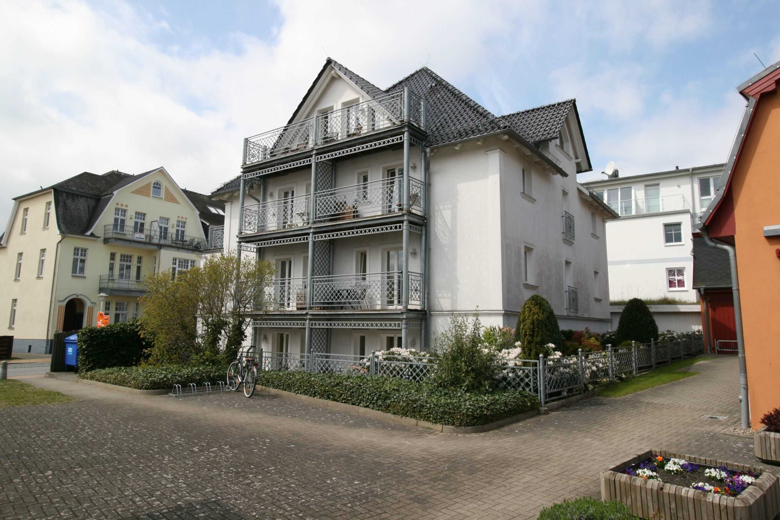 A multi-story residential building with balconies, a brick pathway, and a flower bed.