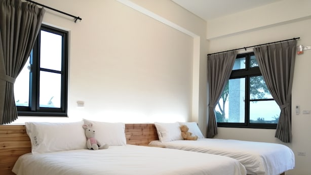 Habitación de hotel con dos camas, cabeceros de madera, ropa de cama blanca y vistas a árboles a través de las ventanas.