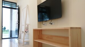 Una habitación moderna con un televisor de pantalla plana grande montado en la pared, una mesa consola de madera, una escalera blanca y un peluche en un estante.