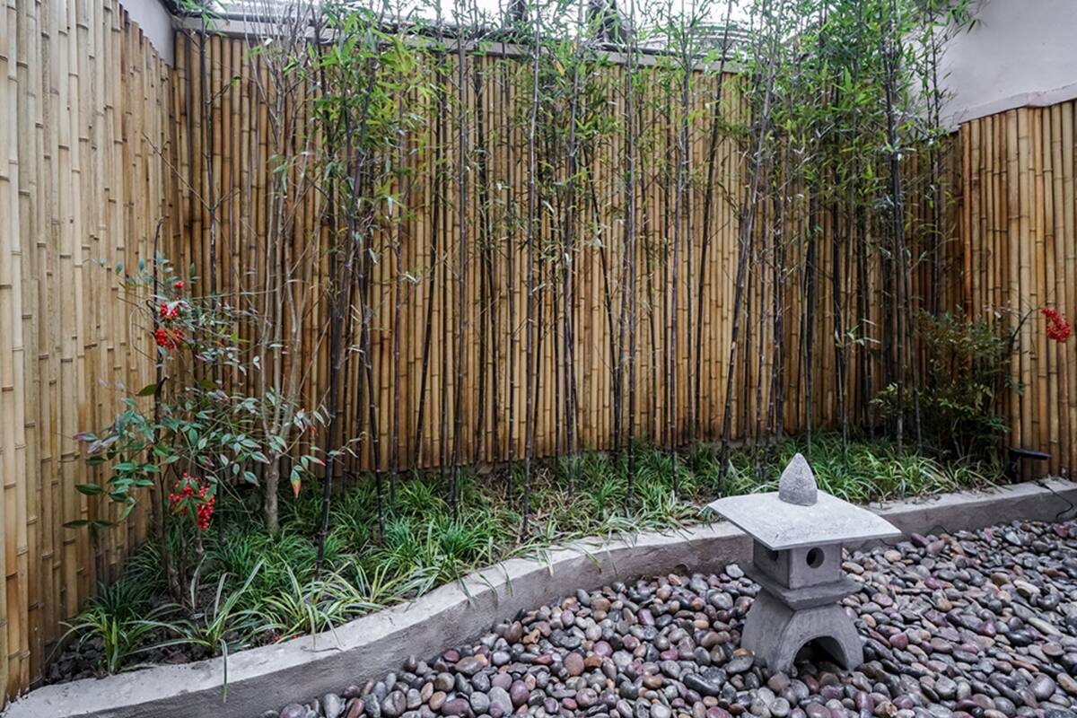Una staccionata di bambù, un abbeveratoio in pietra e un vialetto in ghiaia in un giardino.