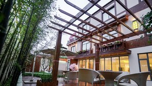 Une terrasse extérieure dotée d’un plancher en bois, de meubles en osier et d’une structure en forme de pergola.