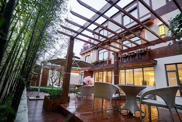 An outdoor patio with wooden flooring, wicker furniture, and a pergola structure. - Yuanli Wafu Guesthouse (Shanghai)