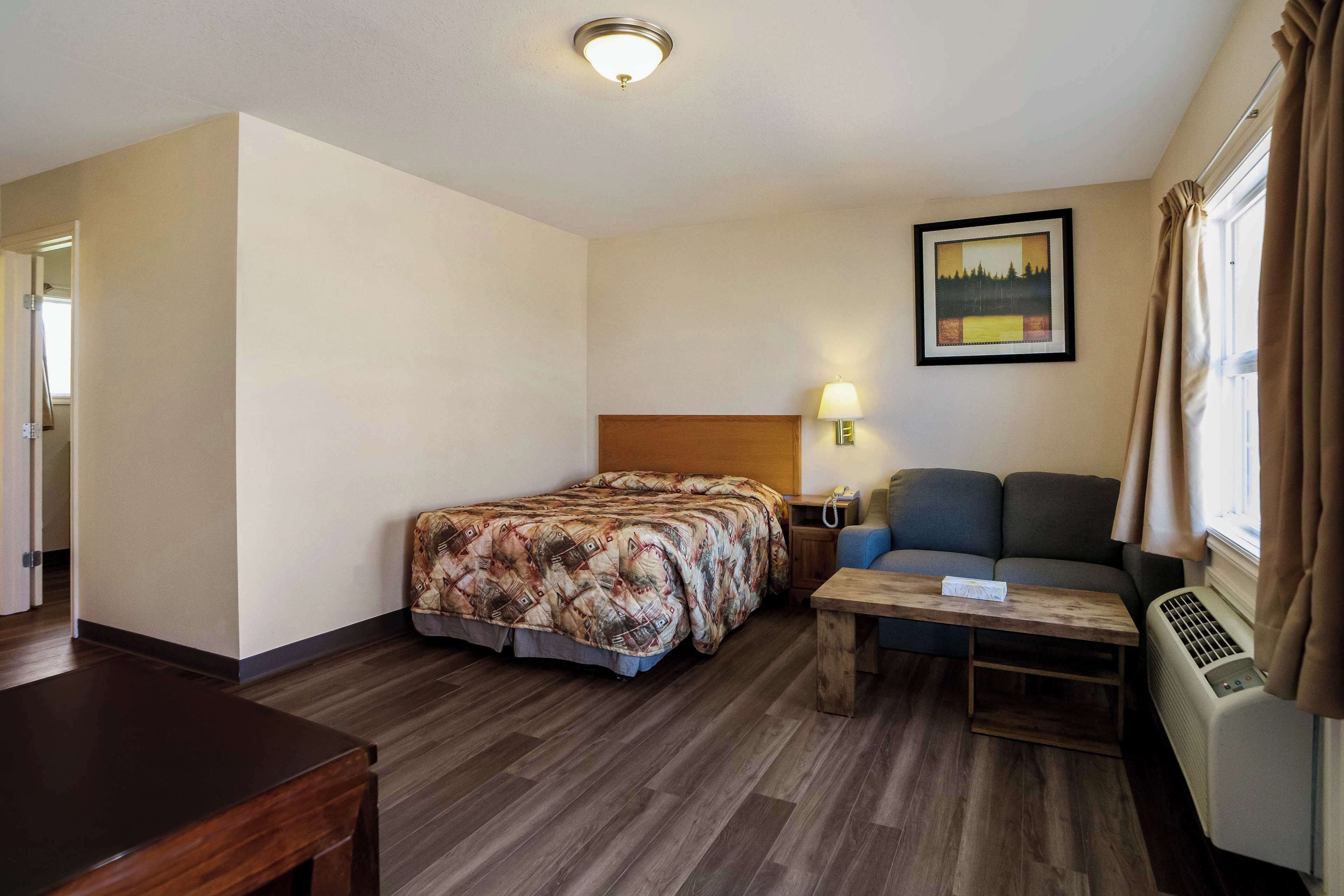 A hotel room with a bed, a sofa, a small table, a lamp, and a picture on the wall.