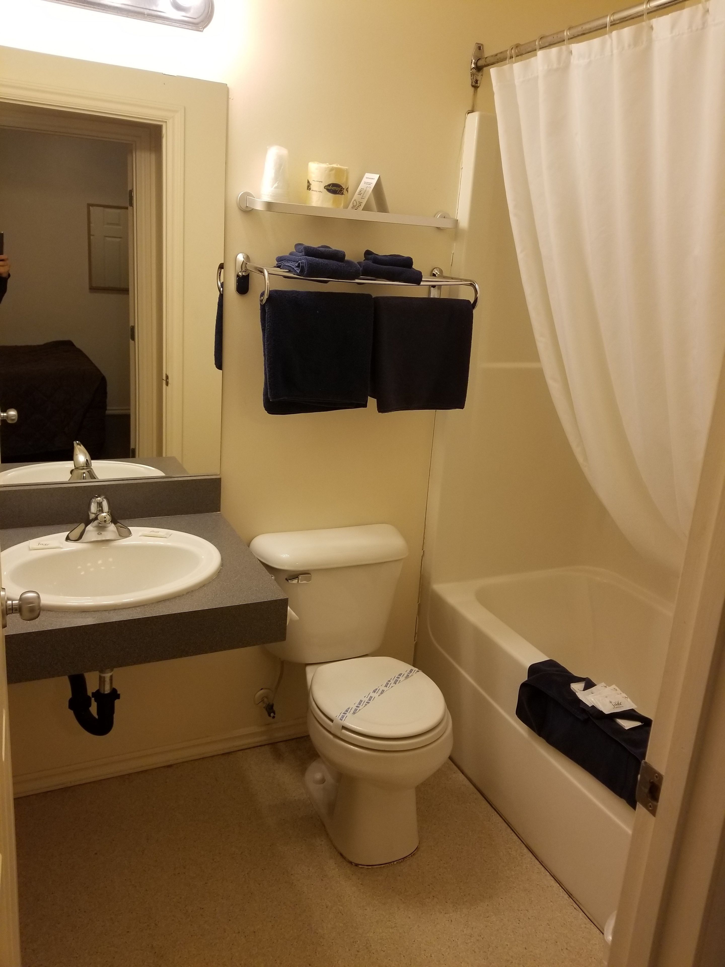 A bathroom with a sink, toilet, and bathtub. There are towels and toiletries on a shelf.