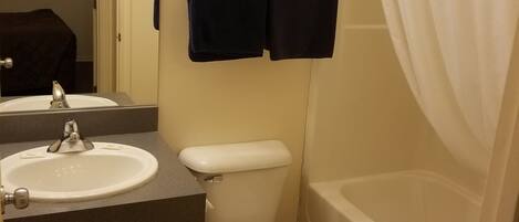 A bathroom with a sink, toilet, and bathtub. There are towels and toiletries on a shelf.