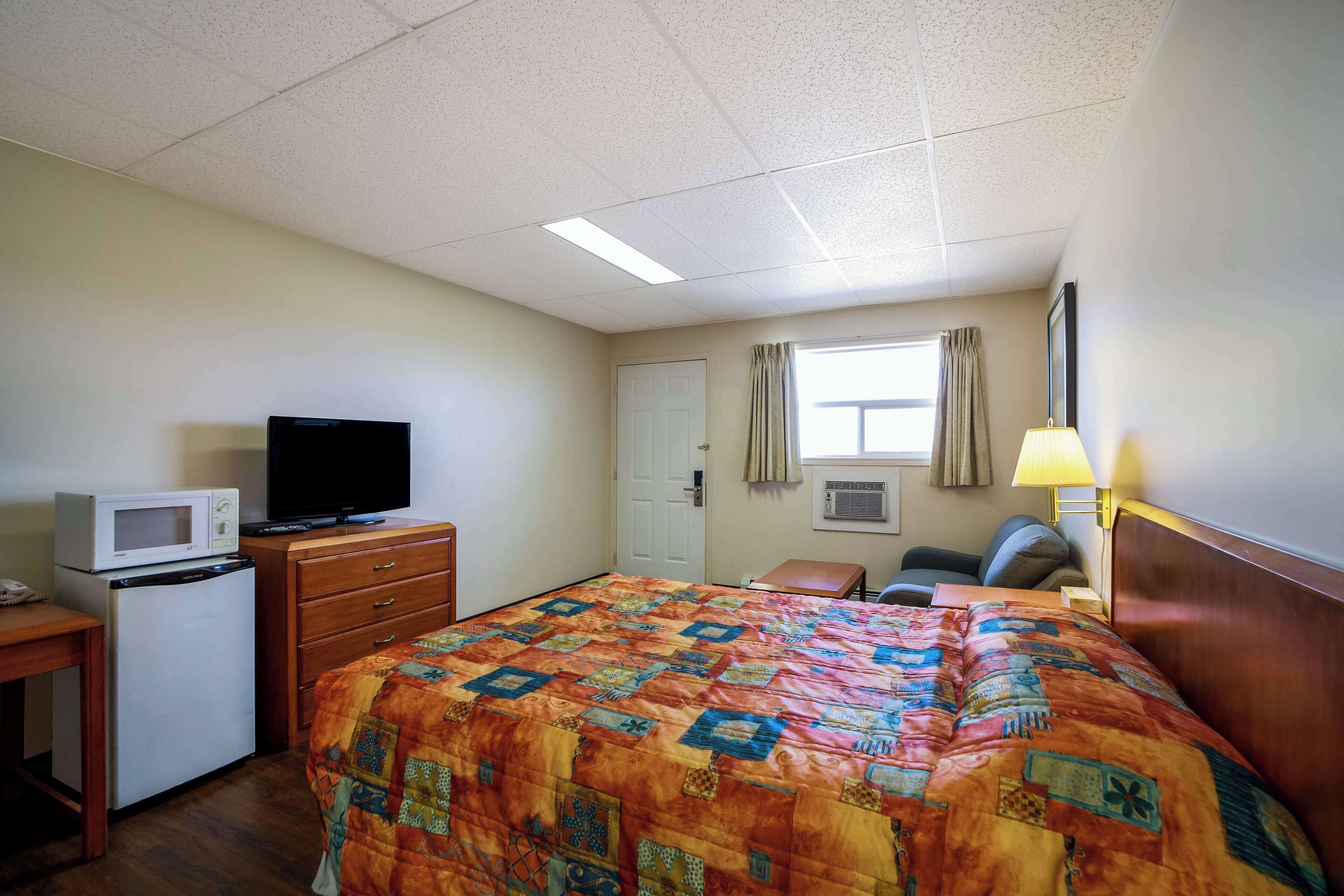 A hotel room with a bed, a desk with a microwave, a television, a chair, a lamp, and a window with curtains.
