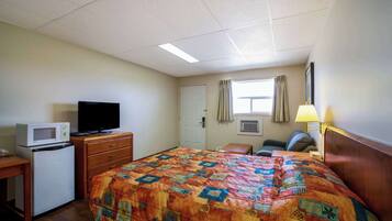 A hotel room with a bed, a desk with a microwave, a television, a chair, a lamp, and a window with curtains.