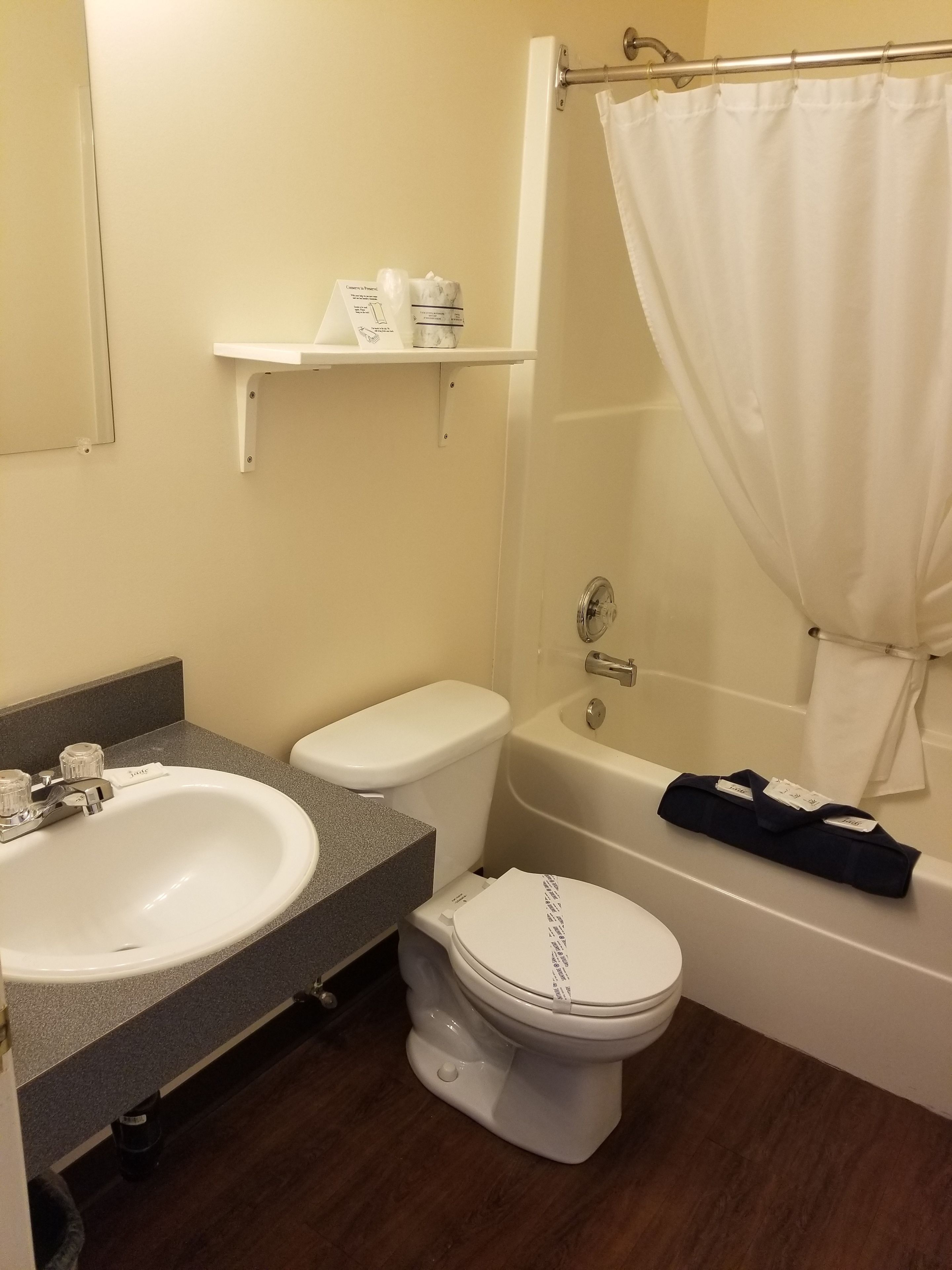 A bathroom with a white sink, toilet, and bathtub. There is a shelf above the sink with toiletries.