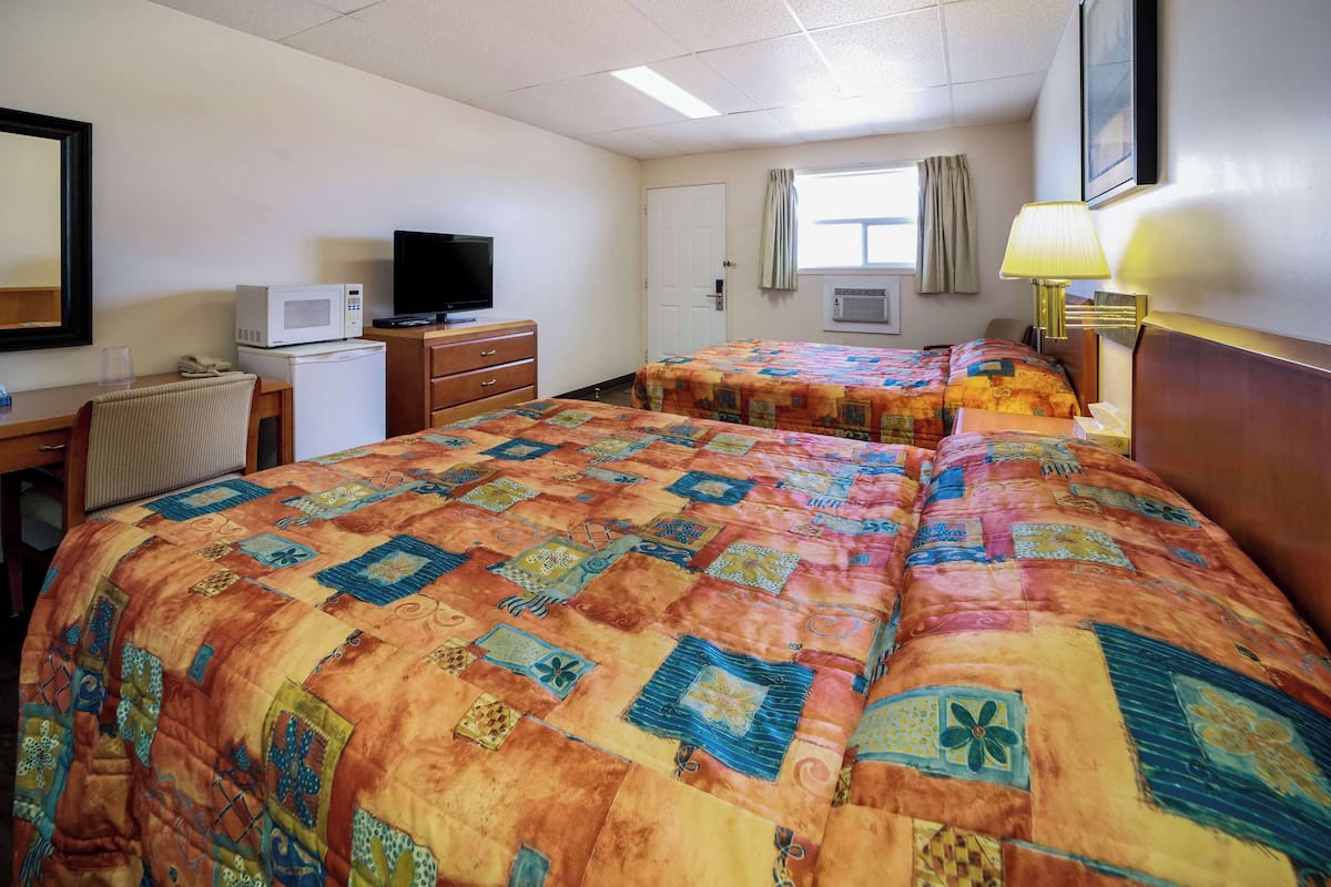 Una habitación de hotel con dos camas, un escritorio, un televisor, un microondas y una lámpara.