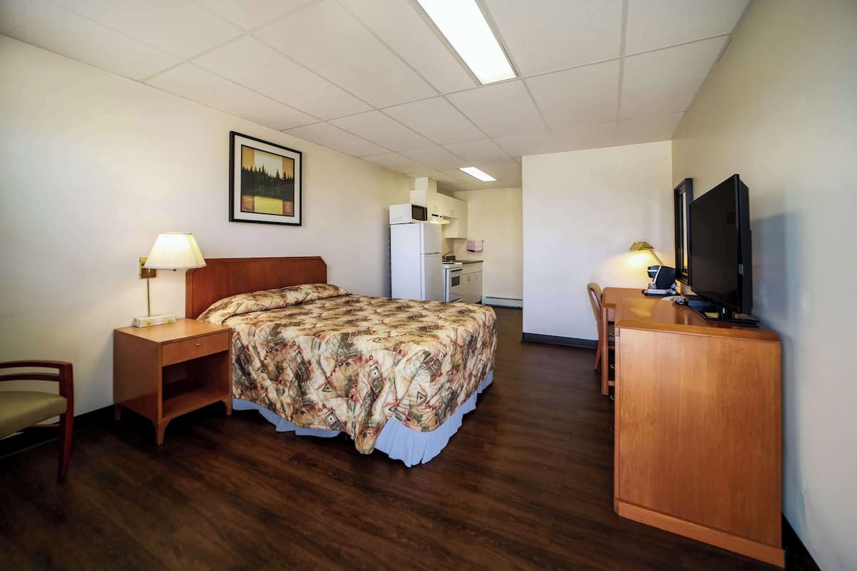 Una habitación de hotel con cama, escritorio, silla, televisión y kitchenette.