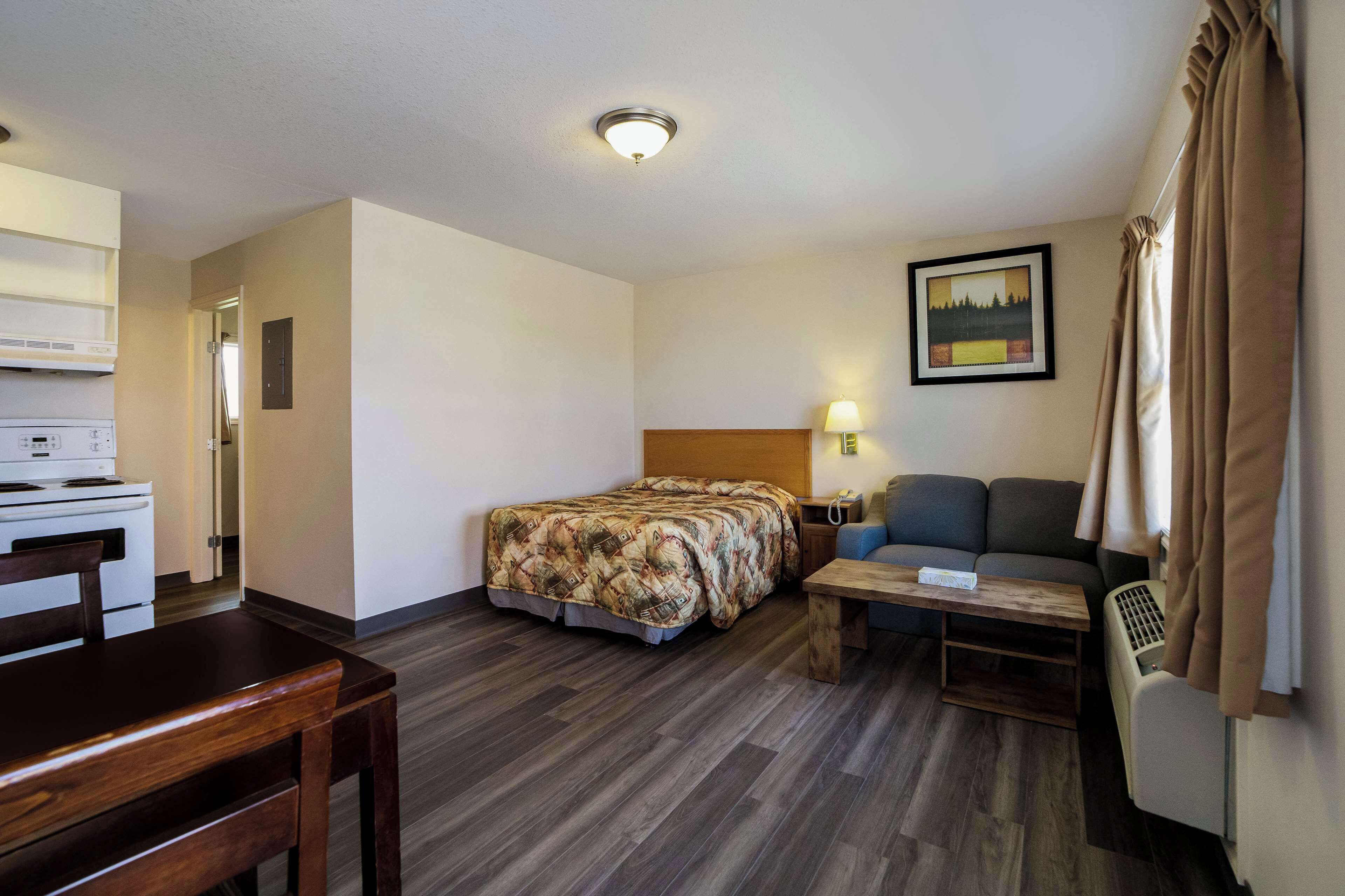 A hotel room with a bed, a sofa, a small table, a desk, a lamp, and a picture on the wall.