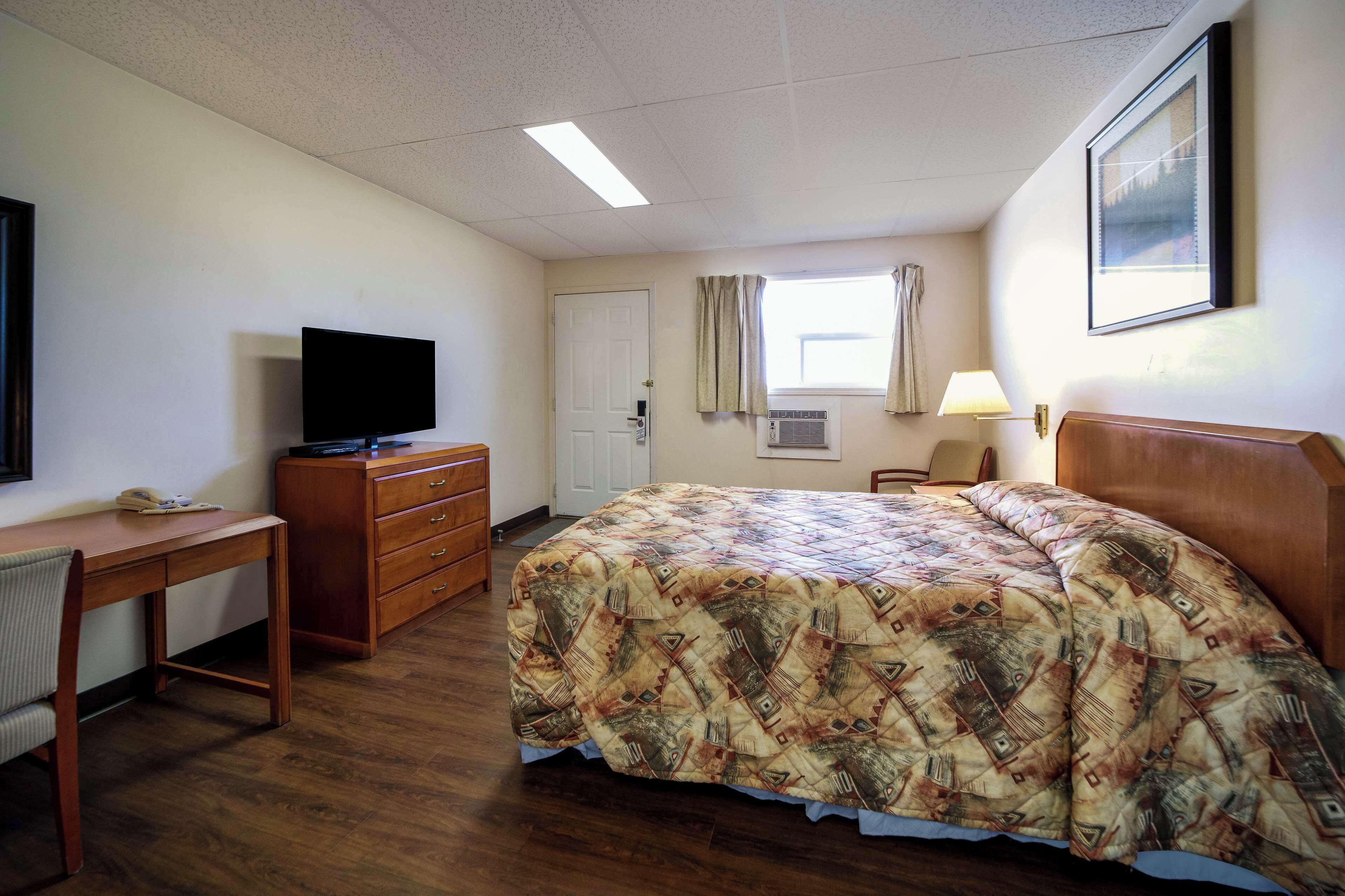 A hotel room with a bed, a desk with a television, a dresser, and a window with curtains.