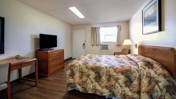 A hotel room with a bed, a desk with a television, a dresser, and a window with curtains.