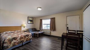 Ett hotellrum med en säng, en soffa, ett litet bord, ett skrivbord, en stol, ett fönster med gardiner, en dörr och en taklampa.