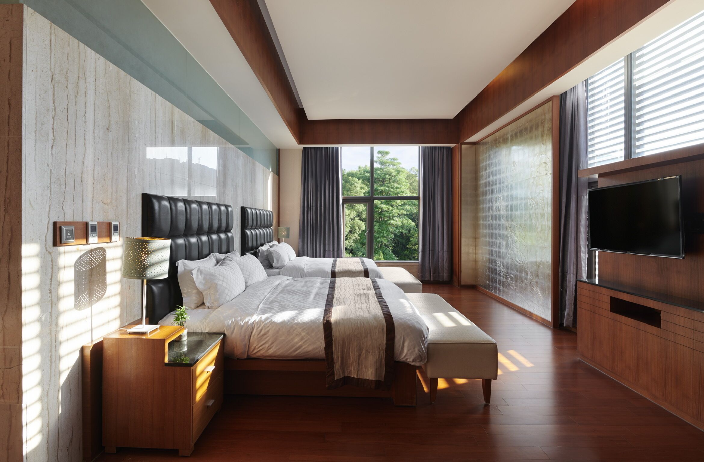 A modern bedroom with a large bed, a TV, and a view of the outdoors.