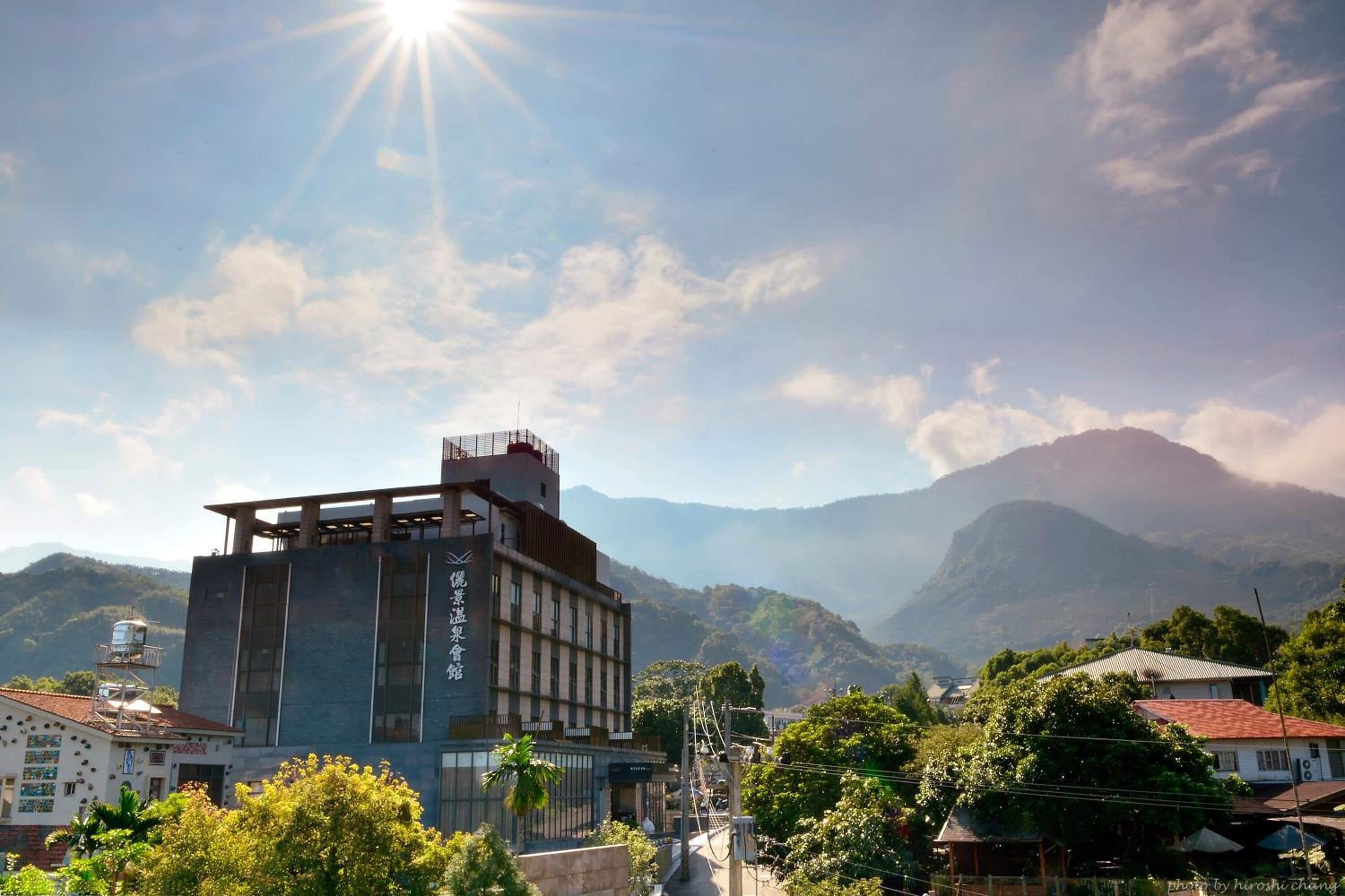 A modern building with a prominent water tower, surrounded by lush greenery and mountains in the background.
