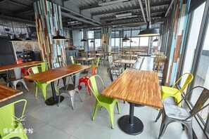 A spacious dining area with multiple wooden tables and chairs, large windows, and exposed ceiling pipes. - Reikei Hot Spring Resort (Tainan)