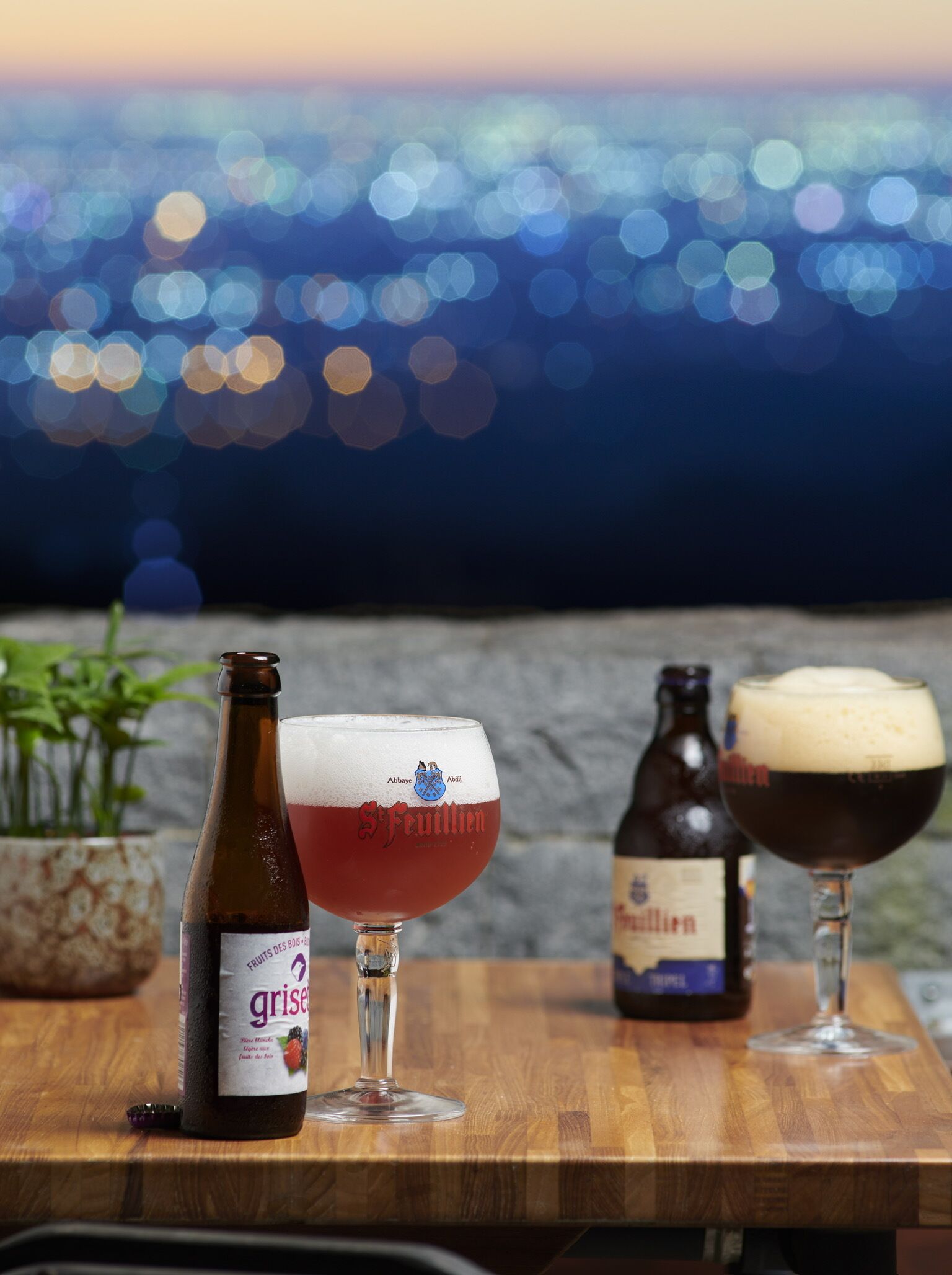 Una mesa de madera con tres botellas y vasos de cerveza, sobre un fondo difuminado de un paisaje urbano.