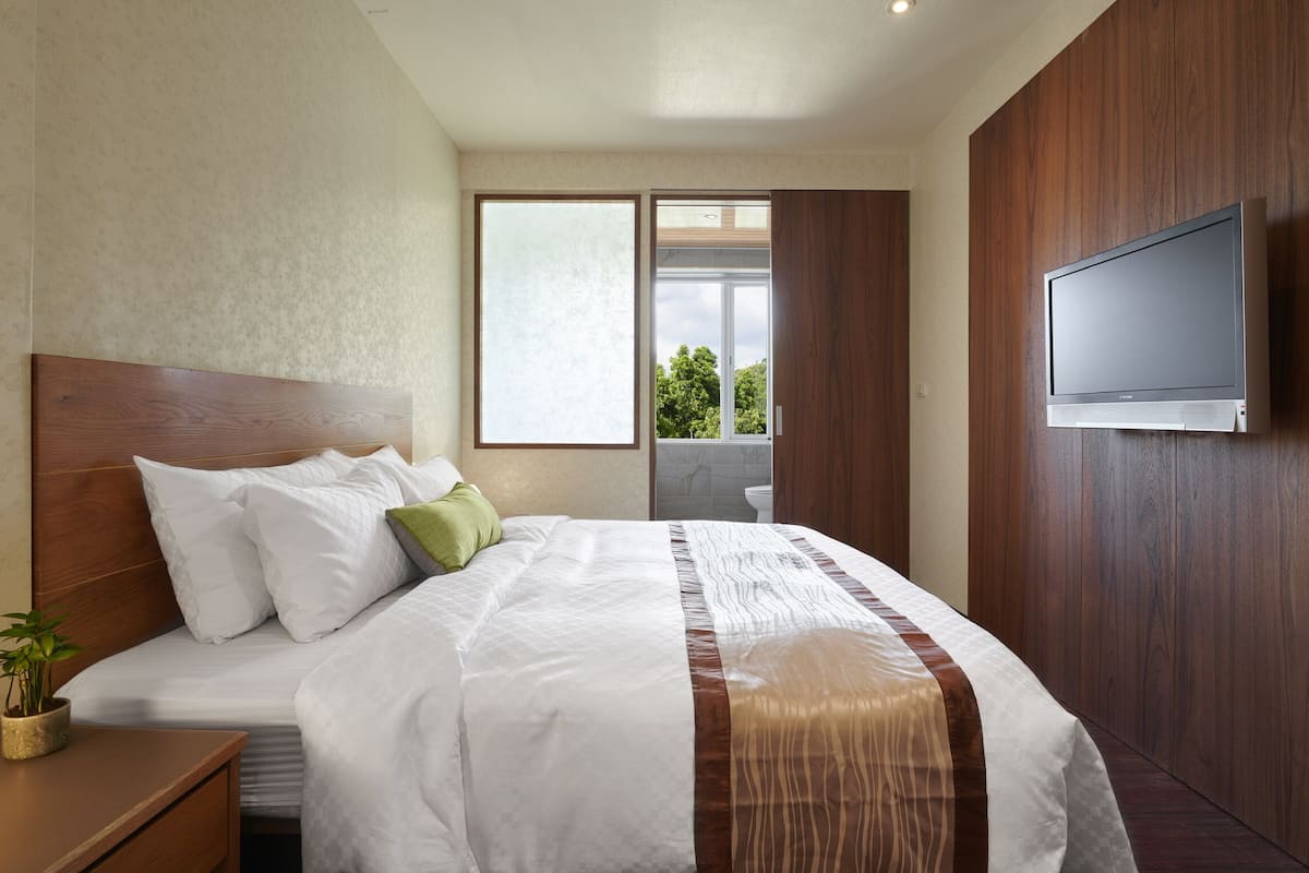 Ein Hotelzimmer mit einem großen Bett, einem an der Wand montierten Fernseher und einem Fenster mit Blick auf Grünflächen.