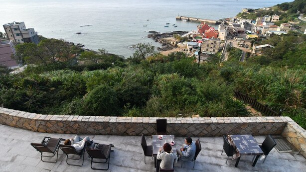A terrace with stone walls, outdoor seating, and a view of the sea and coastal town. - Matsu A Nan Jing B&B (Beigan)