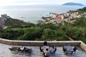 Une terrasse avec des murs en pierre, des sièges extérieurs et une vue sur la mer et la ville côtière.