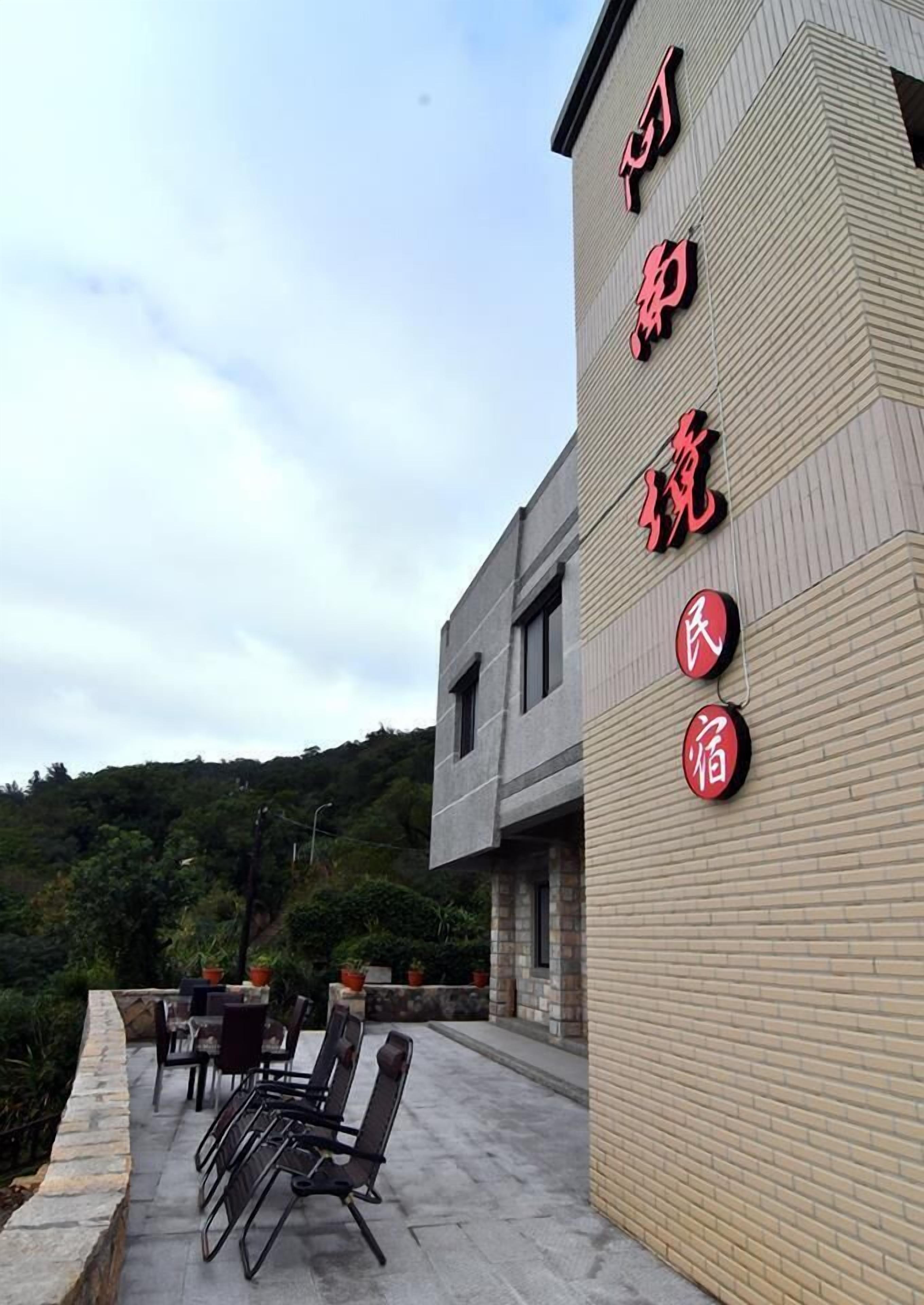 A building with Chinese characters on the facade, outdoor seating, and a view of a hillside.