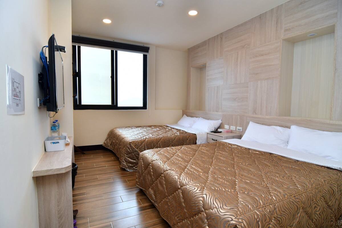 Habitació d'hotel amb dos llits, sòl de fusta, finestra gran i panell de paret de fusta.