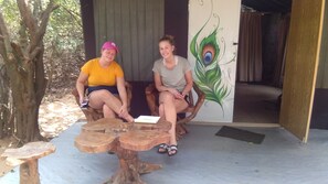 Deux personnes sont assises sur des chaises en bois, devant un bâtiment orné d’une fresque représentant des plumes de paon.