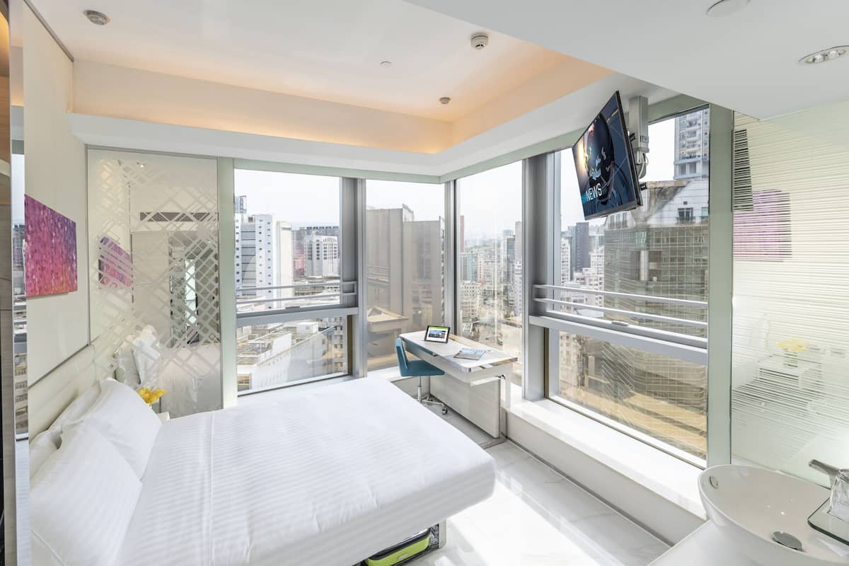 A modern hotel room with a large bed, a desk, and a view of the city.