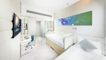 A modern hotel room with a bed, a desk with a laptop, a chair, and a large abstract painting on the wall.