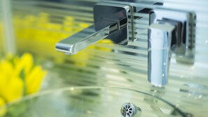 Un grifo moderno de metal con un diseño elegante, colocado sobre una superficie de vidrio transparente.