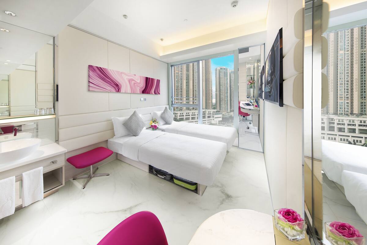 A modern hotel room with a large bed, a sitting area, a bathroom with a vanity, and a view of high-rise buildings.