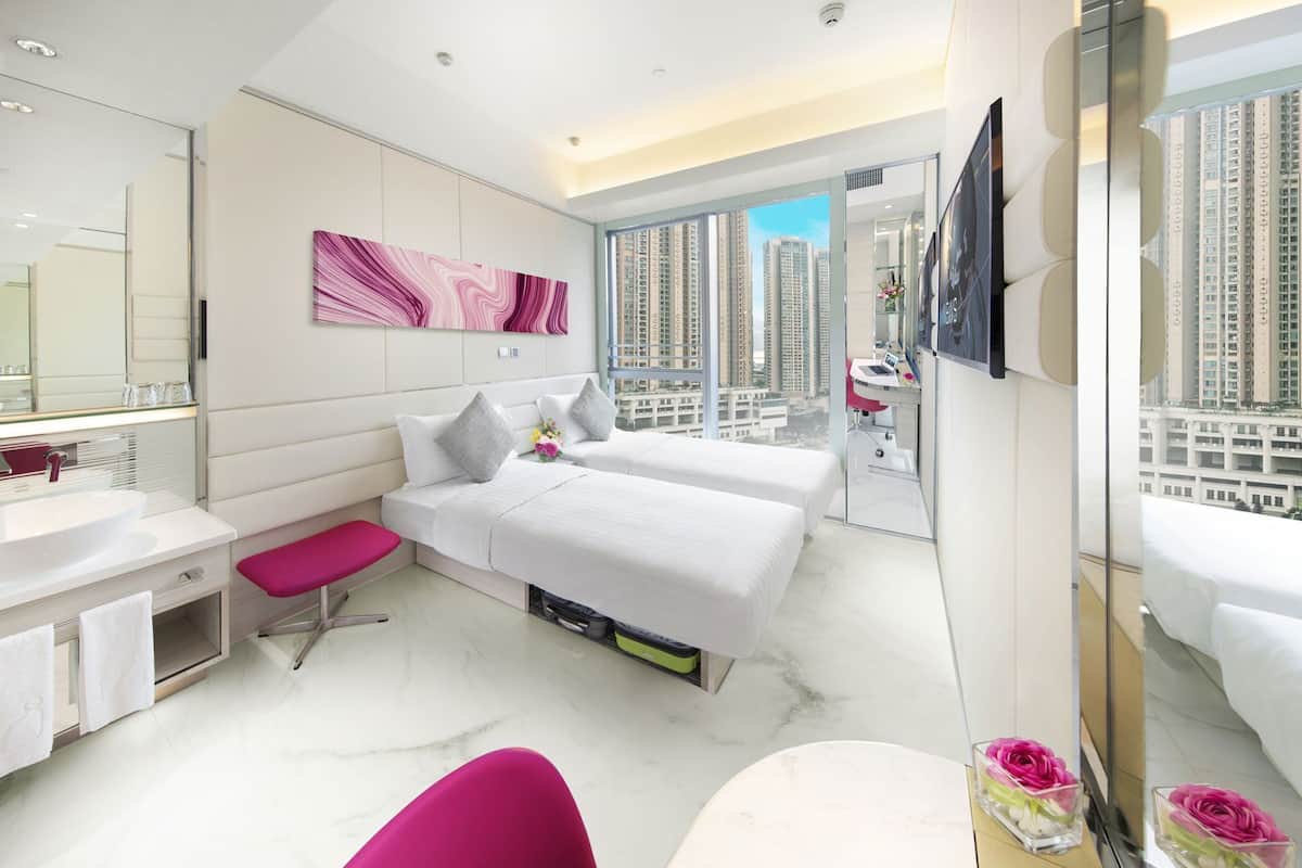 A modern hotel room with a large bed, a separate sitting area, a bathroom with a large mirror, and a city view.