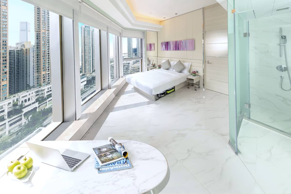 A modern bedroom with a large bed, a glass-enclosed shower, and a laptop on a marble table.