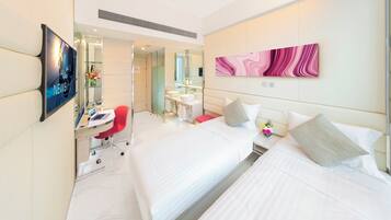 A hotel room with two beds, a desk with a laptop, a TV, a bathroom with a mirror, and a pink abstract painting on the wall.