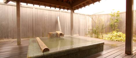 Un jacuzzi bajo una pérgola de madera, con un piso de madera y una cerca de madera al fondo.