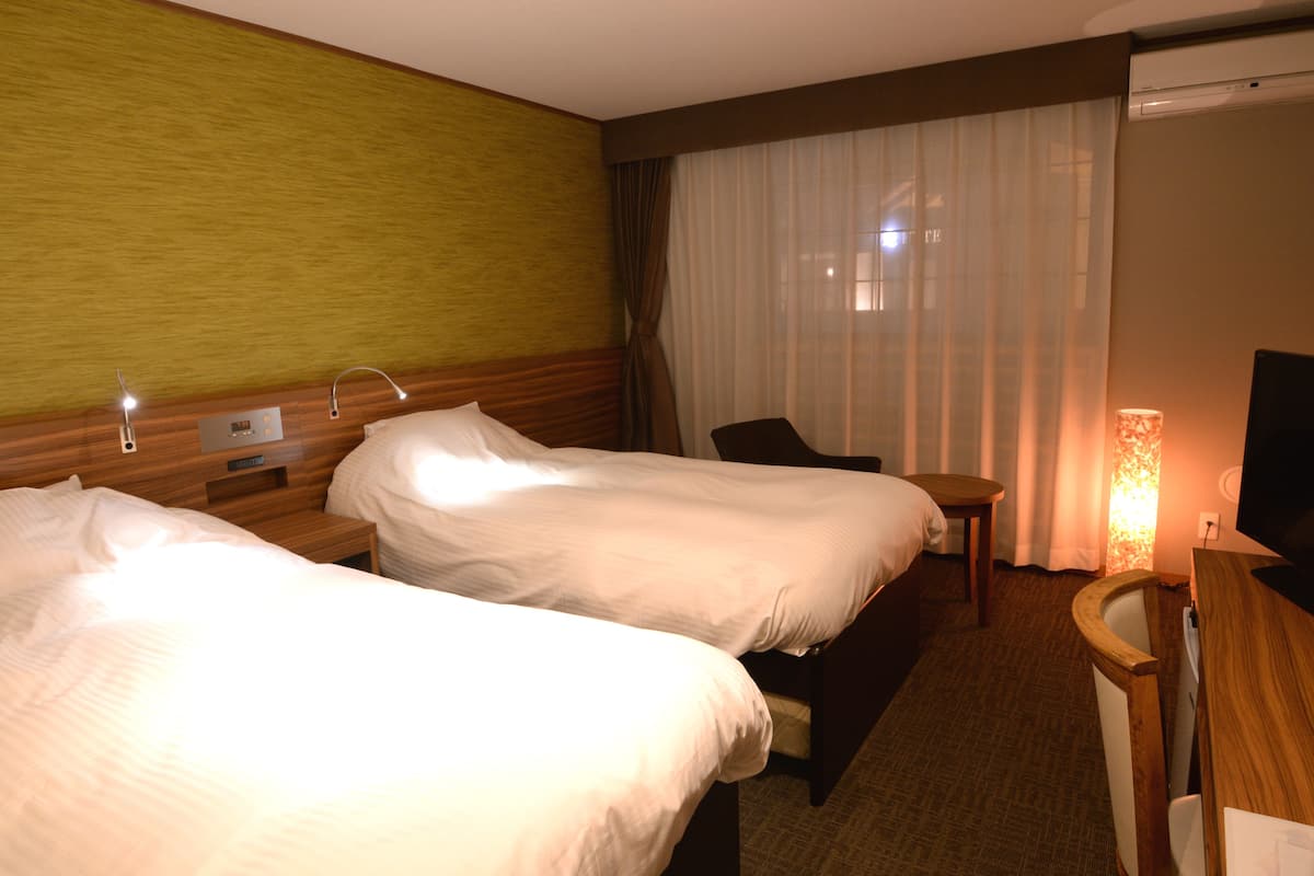 Una habitación de hotel con dos camas, un escritorio, una silla, un televisor y una lámpara.
