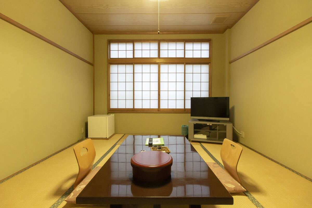 Una habitación japonesa tradicional con tatamis, una mesa baja de tatami y un televisor sobre un soporte.
