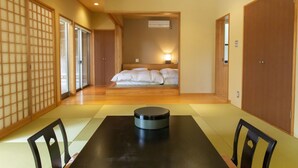 Ein traditioneller japanischer Raum mit Tatami-Boden, einer Futon-Liege, einer Schiebetür und einem Tisch mit einem runden Gegenstand in der Mitte.