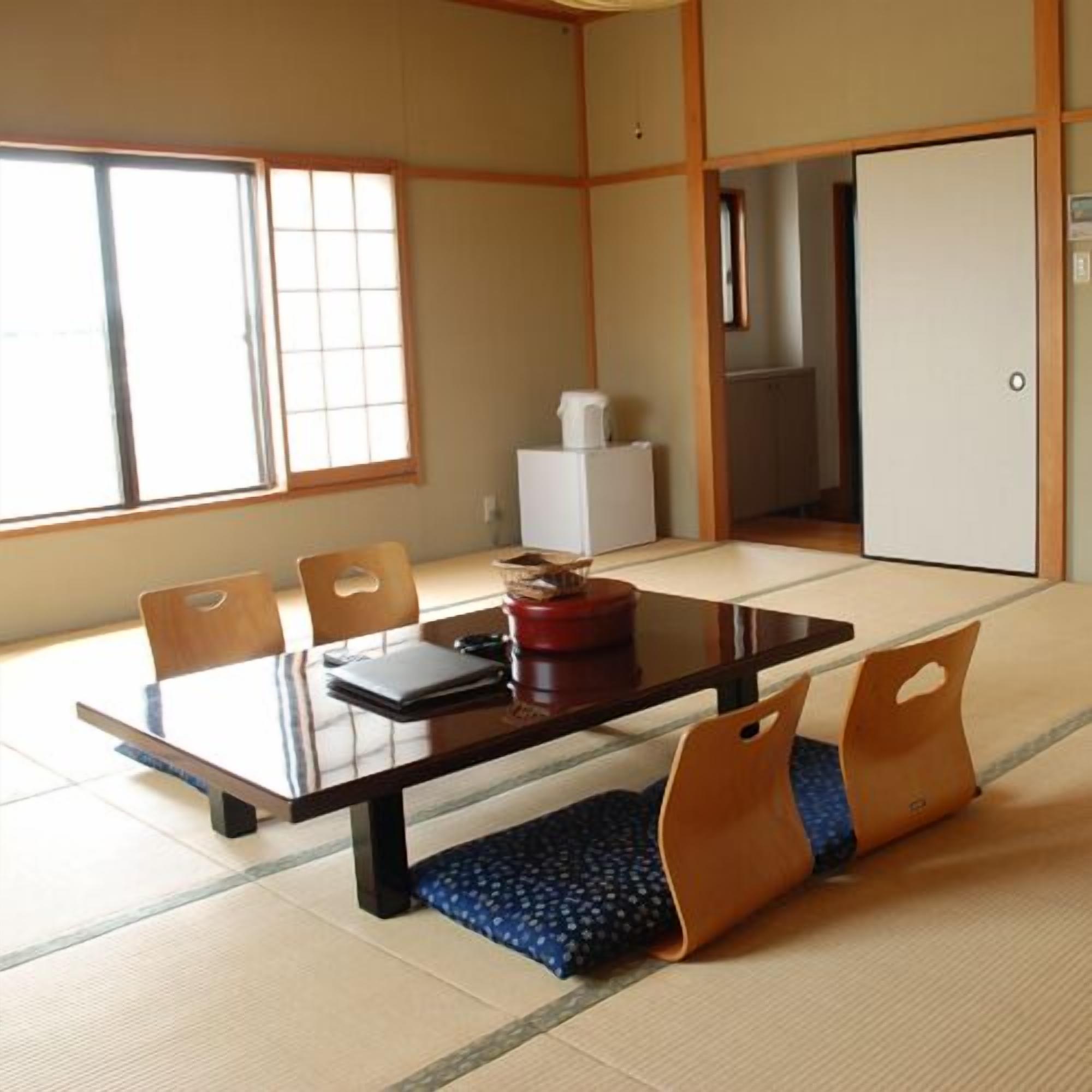Una habitación japonesa tradicional con tatami, una mesa baja, sillas y un puertas correderas.