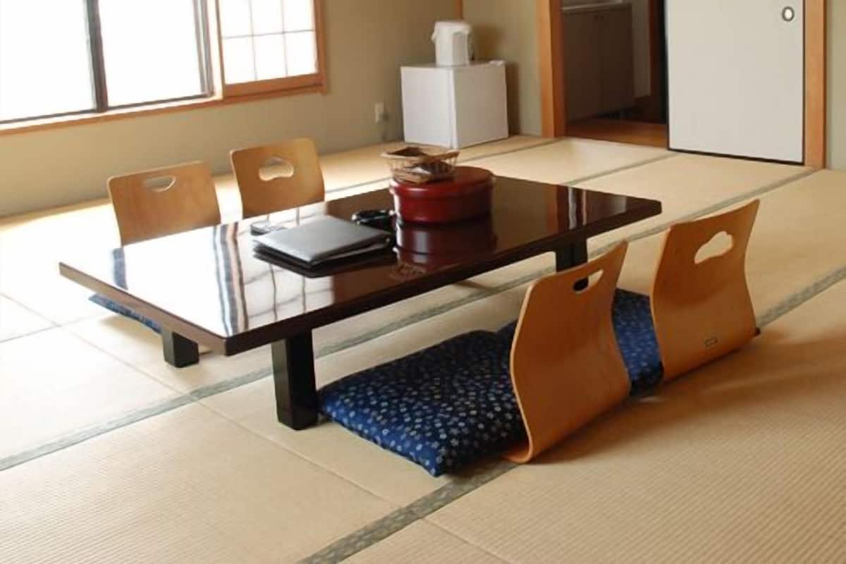 Una habitación japonesa tradicional con tatami, una mesa baja, sillas y un puertas correderas.