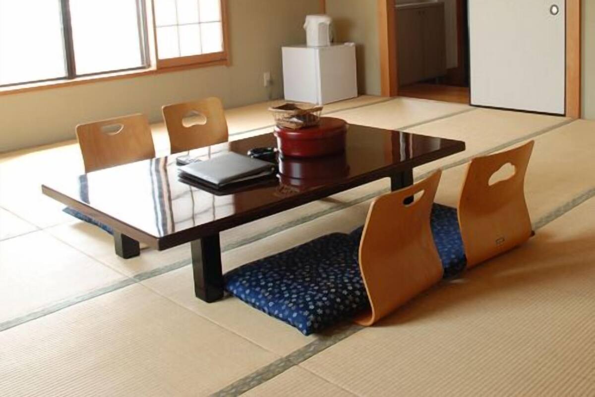 Una habitación japonesa tradicional con tatami, una mesa baja, sillas y un puertas correderas.