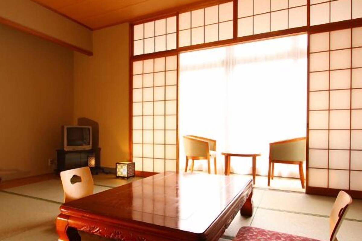 Una habitación japonesa tradicional con suelo de tatami, una mesa de madera baja, dos sillas y un televisor.