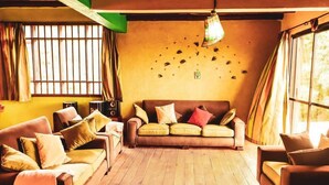 A cozy living room with a brown sofa, yellow cushions, and a wooden floor. - Kamaki House (Naivasha)