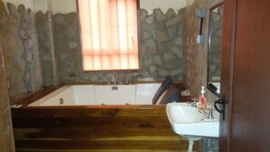 A bathroom with a stone wall, a wooden bench, a bathtub, and a sink with a mirror. - Kamaki House (Naivasha)