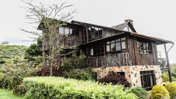 A rustic wooden house with a stone foundation, surrounded by lush greenery and a well-maintained garden. - Kamaki House (Naivasha)