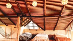 A room with a sloped wooden ceiling, three beds, a hammock, and hanging light fixtures. - Kamaki House (Naivasha)