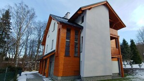 Una casa moderna de madera de dos pisos con un balcón, rodeada de árboles y un paisaje nevado.
